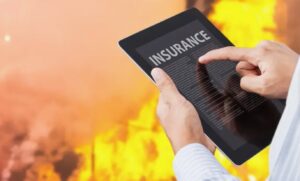 Person reviewing digital wildfire insurance policy on tablet with flames in background