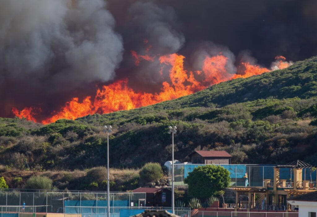 Intense wildfire flames approaching hillside buildings and recreational facilities