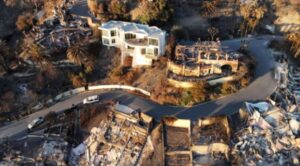 Aerial view of a modern home intact while surrounding houses are burned in a California wildfire.