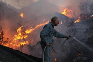 Man using hose as wildfire burns through dry hillside