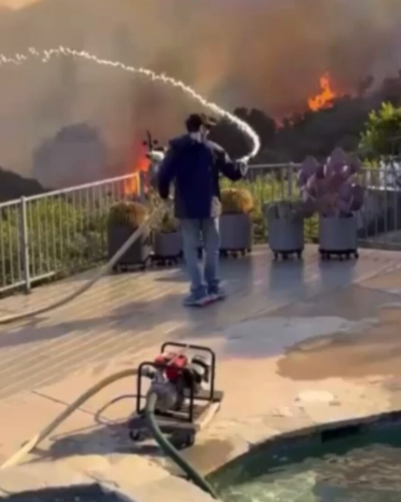 Man using a pump and hose to spray water from pool toward wildfire